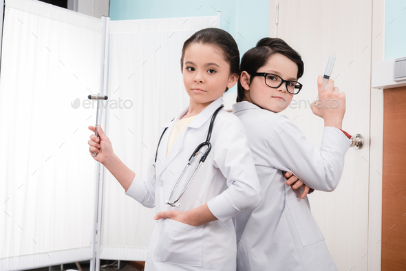 Kids in medical uniform holding syringe and reflex hammer looking at camera