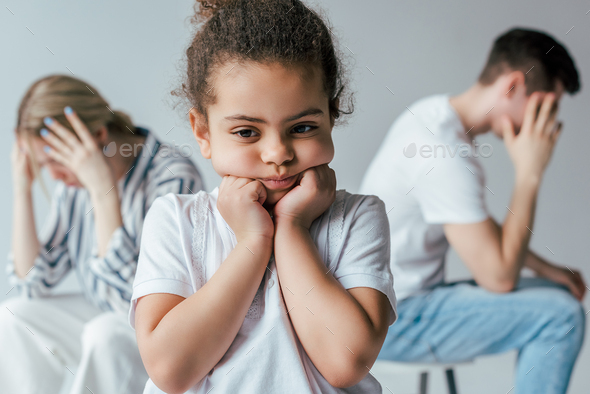 selective focus of sad african american kid touching face near divorced foster parents isolated on