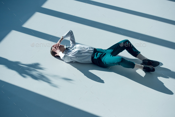 young stylish hipster woman in white shirt and green trousers lying on floor with hands on eyes
