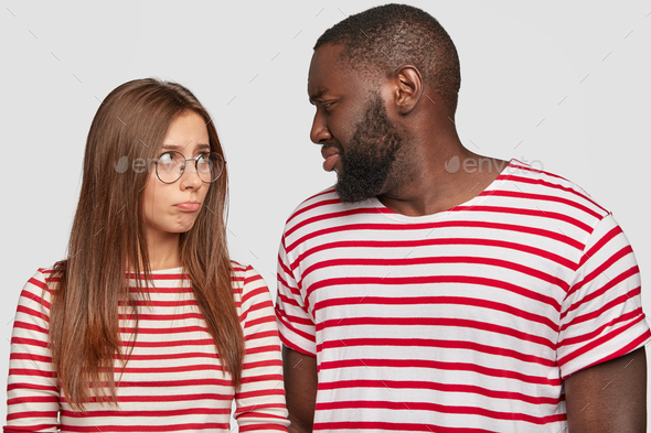 Photo of mixed race couple sort out relationships, look in displeasure at each other, have quarrel,