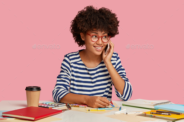 Successful architect draws, has phone conversation with someone, cheerful expression, wears red rim