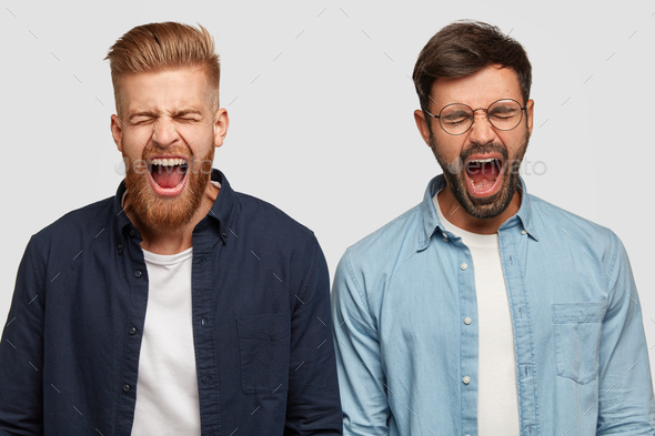Photo of annoyed guys produce loud yell, open mouth widely, have trendy haircut and bristle, stand s
