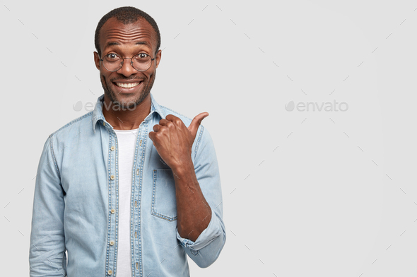 Studio shot of handsome cheerful dark skinned man with toothy smile, shows new item, has shining tee