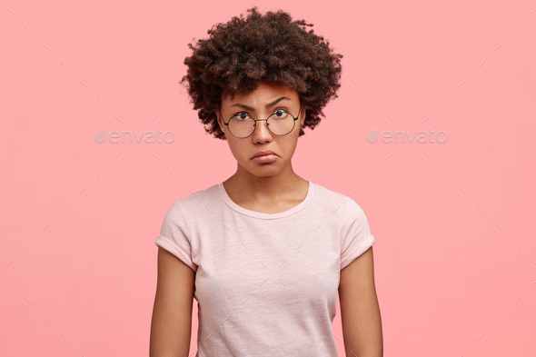Waist up portrait of dissatisfied African American female with negative angry facial expression, loo