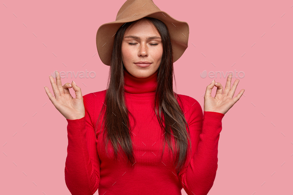 Everything is perfect. Relaxed freckled woman dressed in hat and red turtleneck sweater, demonstrate