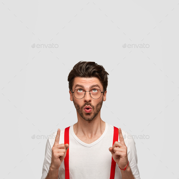 Attractive fashionable guy with trendy hairstyle, keeps mouth round, points with both index fingers