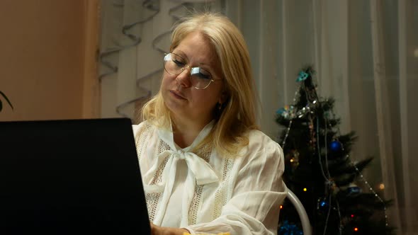 Caucasian blonde woman over 40 works at home on a computer during the holidays alt