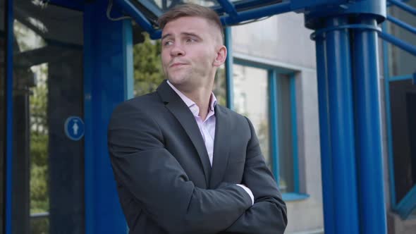 Handsome Caucasian Man in Suit with Crossed Hands Standing at Business Center Entrance Waiting alt