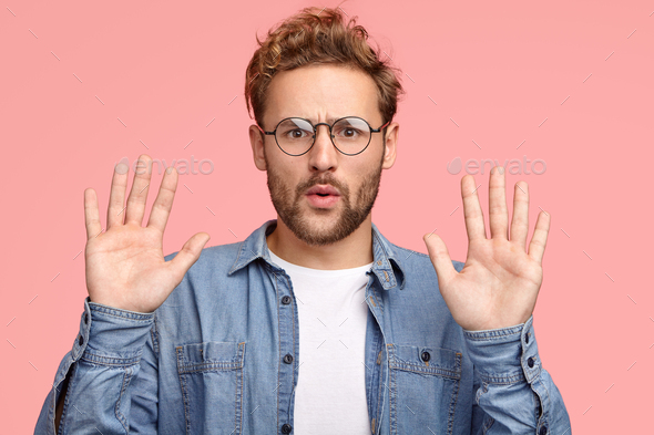 Calm down, please! Handsome unshaven Caucasian man keeps palms in front, asks to leave him in peace