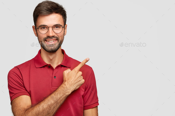Happy smiling European male with bristle, points with index finger aside, invites you to have dinner