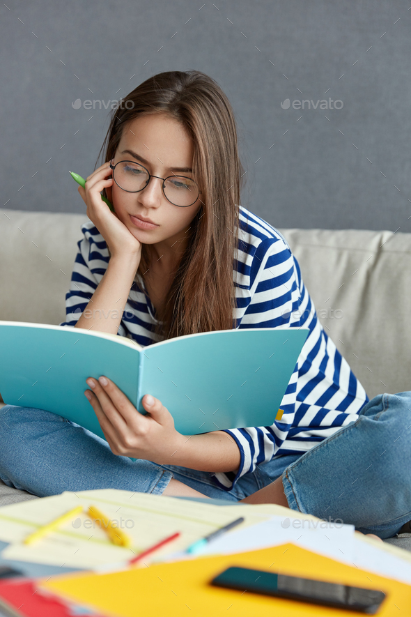 Concentrated woman in optical glasses, thinks on creative ideas for publication, holds pen for writi - Stock Photo - Images
