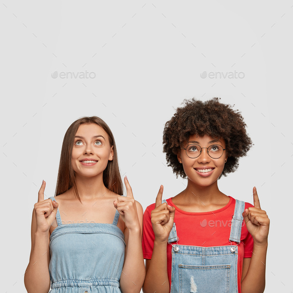 Studio shot of happy mixed race young women dressed in fashionable clothes, show free space above, a