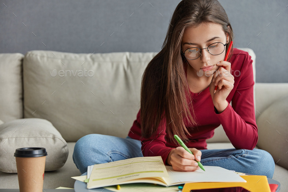 Shot of serious skilled student with pen in hand, writes curriculum vitae, wants to find extra job, - Stock Photo - Images