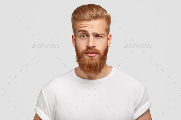 Bewildered man with thick ginger beard, raises eyebrows, reacts on fake news from friend, looks dire