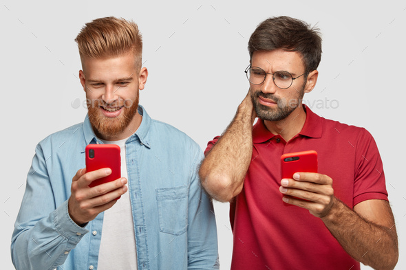 Curious bearded young man peeks at brother`s smart phone, play online games on cell phones, spends l