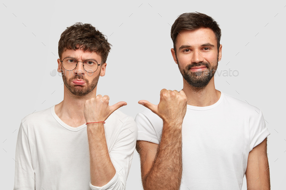 Displeased bearded male feels offended of bad jokes of his friend, point at each other, argue about