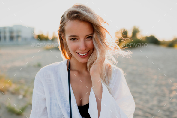 Pretty blonde woman in white blouse on the beach.