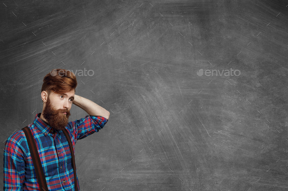 Confused bearded man scratching his head. Stylish student wearing flannel checkered shirt having for