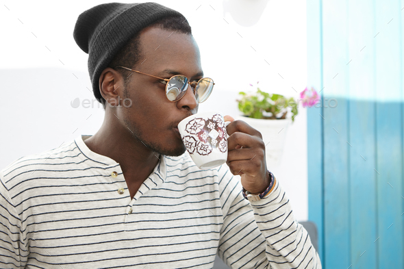 Confident young Afro American male student dressed stylishly enjoying coffee at college cafe. Trendy