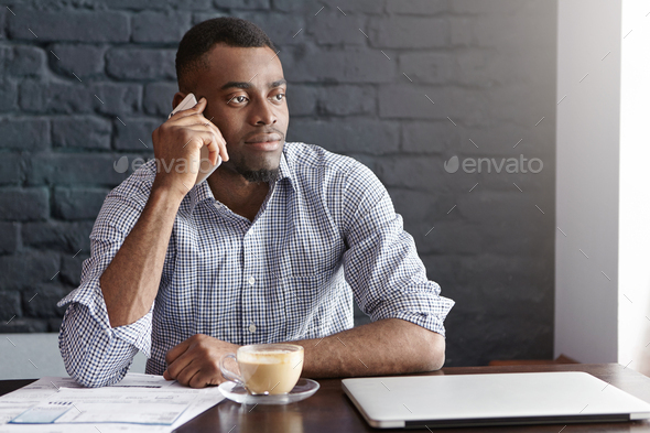 Successful African businessman in shirt with rolled up sleeves having phone call with his partner wh