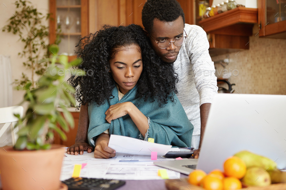 Stressed young African-American couple reviewing family budget and managing finances together at hom