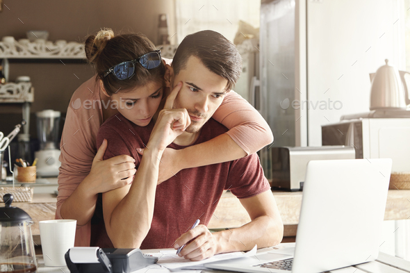 Couple facing financial stress. Young thoughtful bearded man holding index finger on his temple plan