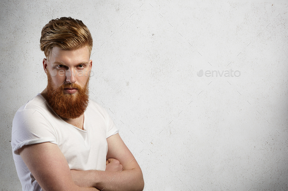 Portrait of stylish redhead hipster with fuzzy beard wearing white t-shirt with rolled up sleeves po