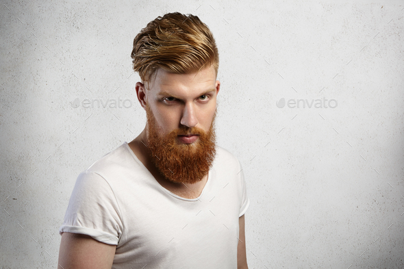 Headshot of self-assured bearded hipster with stylish haircut and muscular build wearing t-shirt wit