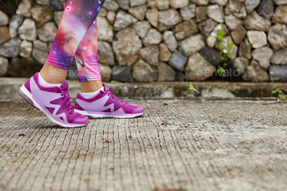 Sports and healthy lifestyle. Close up of woman's legs in stylish purple sneakers and space print le