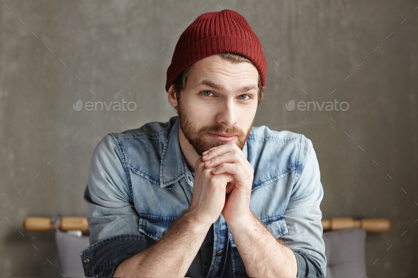 Portrait of good-looking bearded hipster with friendly smile and kind eyes sitting alone in modern c