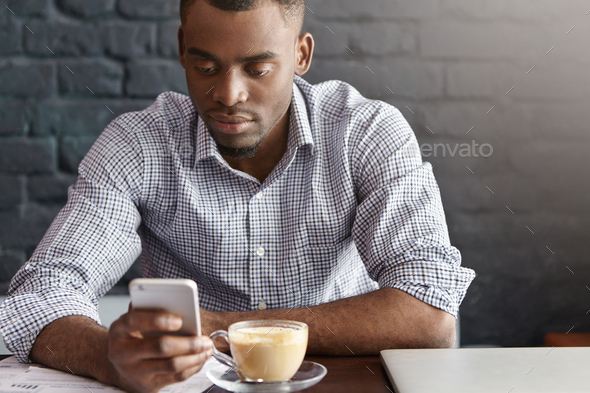 Handsome African office worker wearing checkered shirt with rolled up sleeves enjoying online commun
