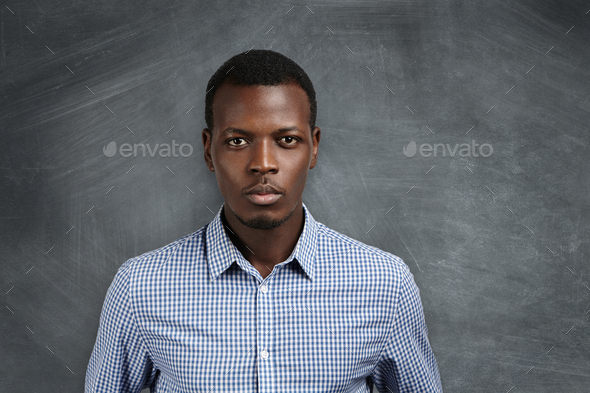 Portrait of handsome young African school teacher wearing checkered shirt getting ready for lesson,