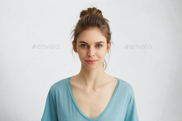 Portrait of beautiful female having blue shining eyes, thin lips, pure skin and dark hair tied in kn