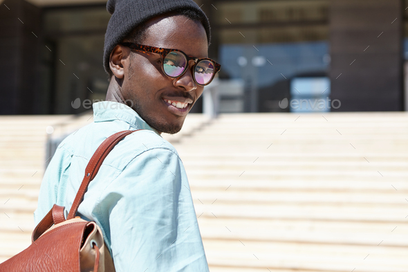 Outdoor portrait of young Afro American traveler with knapsack standing on concrete stairs, going to - Stock Photo - Images