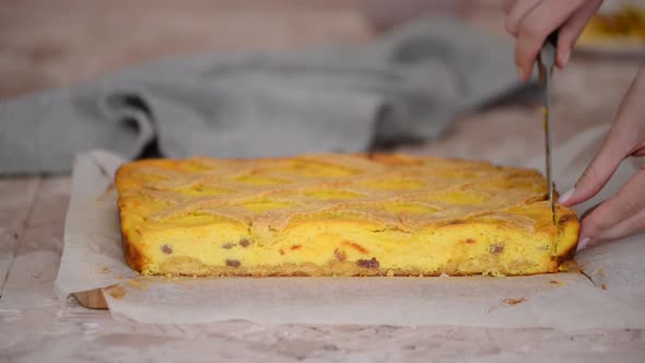 A woman cuts the edges of a traditional Polish cheesecake cake with raisins.