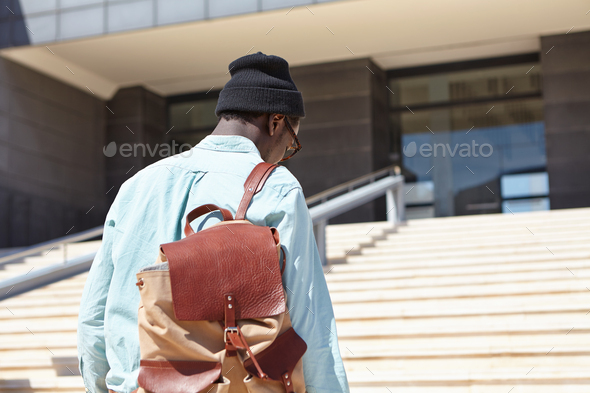 Rear shot of unrecognizable Afro American male student carrying knapsack going upstairs towards mode - Stock Photo - Images