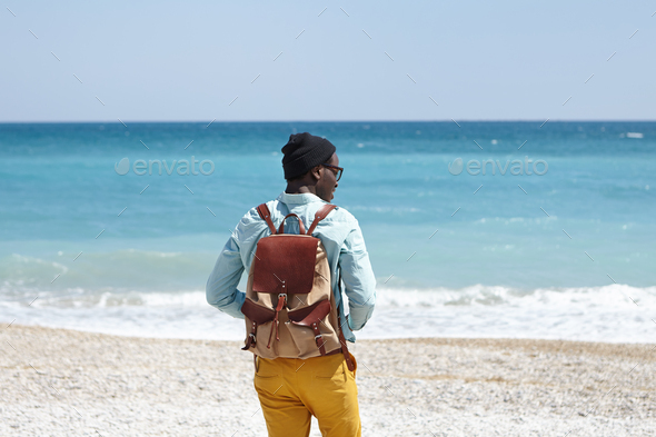 Back outdoor view of young African male tourist with knapsack wearing trendy clothing spending sunny - Stock Photo - Images