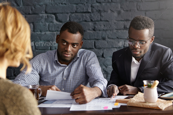 Attractive dark-skinned HR manager reading curriculum vitae in his hands while conducting job interv - Stock Photo - Images