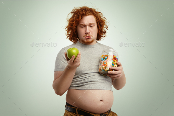 Studio shot of thoughtful indecisive redhead overweight fat man with big stomach feeling confused an
