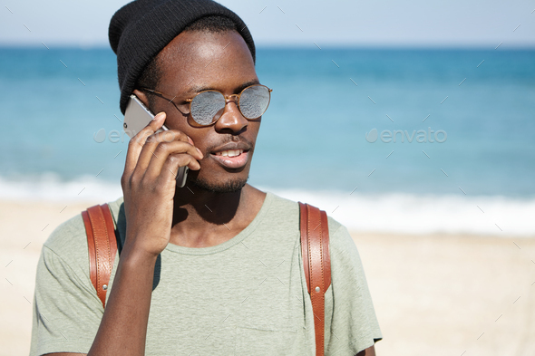 Picture of trendy looking black male tourist with knapsack, wearing hat and sunglasses on sunny weat - Stock Photo - Images
