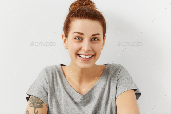 Indoor shot of pretty white red haired woman with tattooed shoulder, beautiful laughing eyes and sli