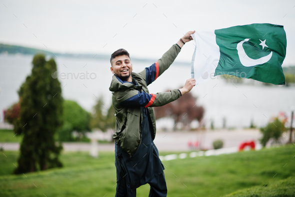 Сonfident pakistani indian muslim arabic boy in grey kameez shalwar suit with Pakistan flag.