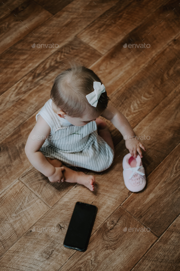 Cute little toddler baby girl with cell phone near on the floor. Vertical portrait of kid sitting on - Stock Photo - Images
