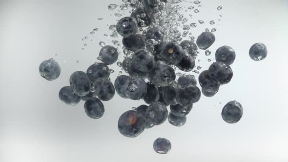 Blueberries fall into the water with splashes and bubbles in slow motion alt