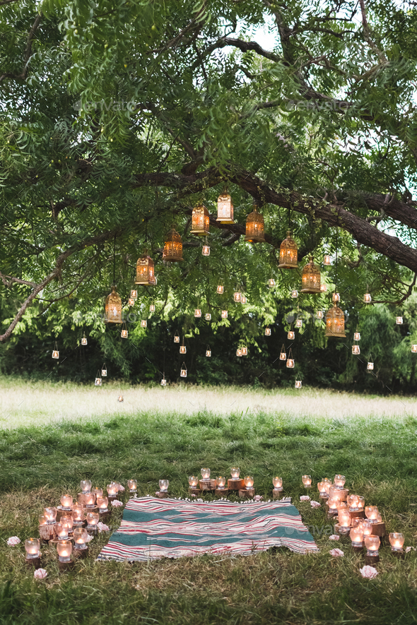 Evening wedding ceremony with a rug and lot of vintage lamps and candles on big  tree. Rustic style Stock Photo by olegbreslavtsev