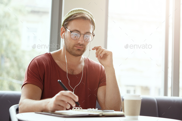 Handsome unshaven successful businessman wears trendy clothes, takes notes, makes list of things to