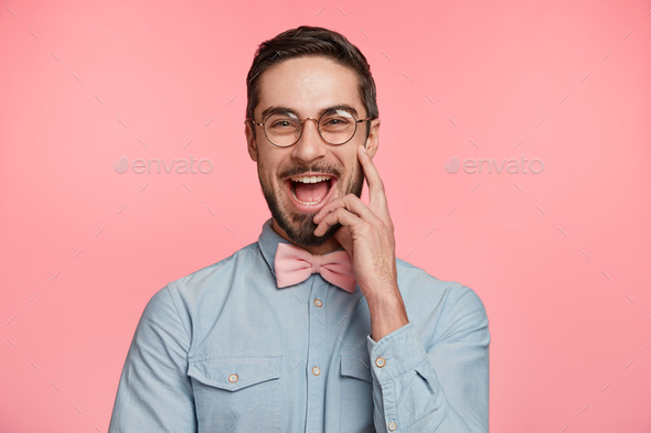 Cheerful joyful male model smiles happily as recieves news about his promotion, invites friends to c