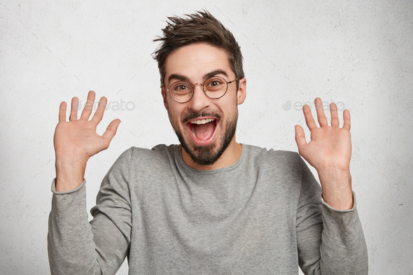 I am not guilty! Cheerful stylish fashionable young hipster guy in eyewear raises hands as shows bei
