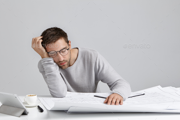 Tired young attractive man sleeps at work place, has much work, being fatigue and exhausted, isolate