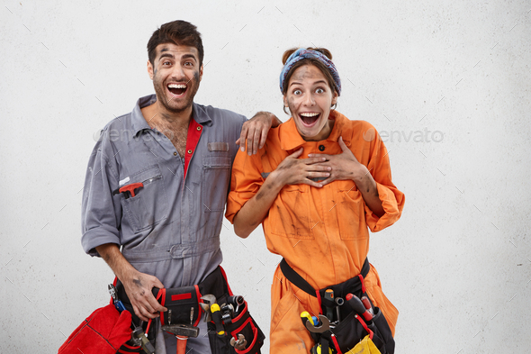 Excited female and male plumbers don`t believe their eyes, look with widely opened mouthes in camera